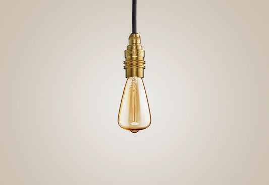 E14 decorative Lightbulb hanging over a light background. The lightbulb is fitted with a Coolicon Brass Suspension Set