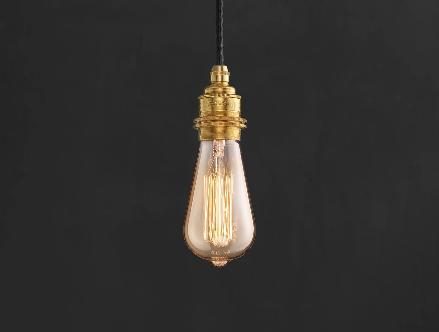E27 decorative Lightbulb hanging over a black background. The lightbulb is fitted with a Coolicon Brass Suspension Set