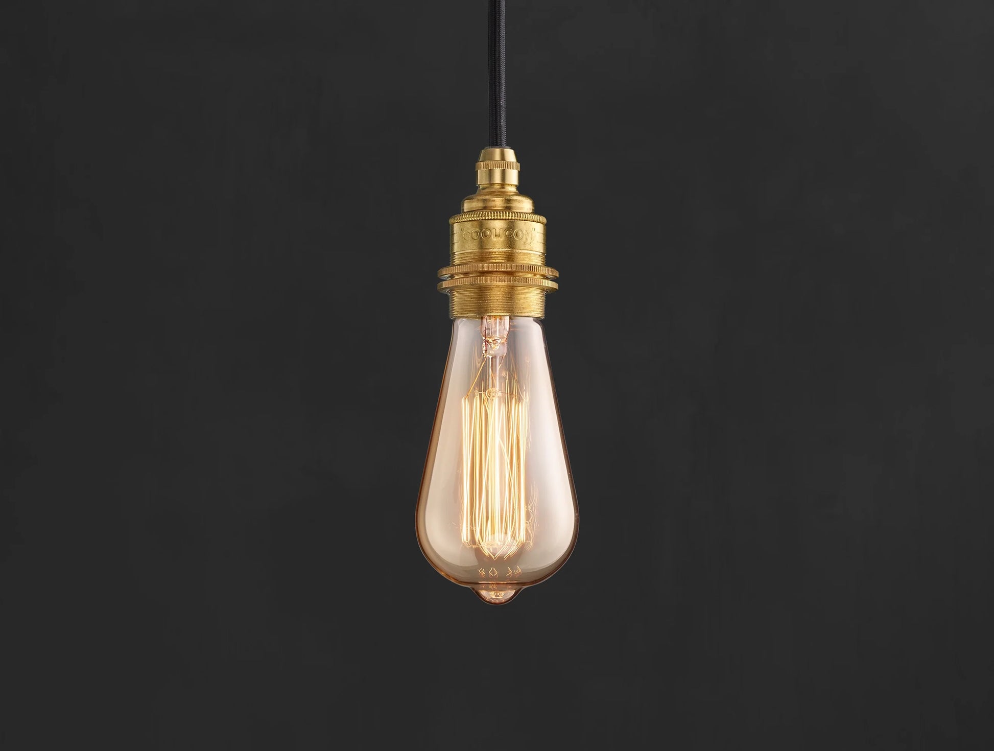 E27 decorative Lightbulb hanging over a black background. The lightbulb is fitted with a Coolicon Brass Suspension Set